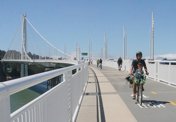 Photo of a parent bicycling on the Bay Bridge east span pathway and carrying a child in a front seat