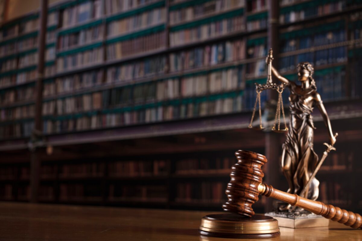 A gavel and justice sculpture, with a law library in the background