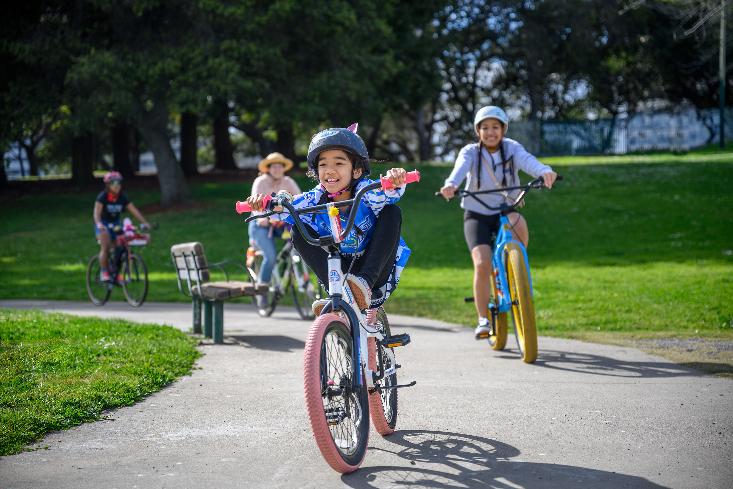 Two kids and two adults riding bikes on a path, wearing helmets and smiling.