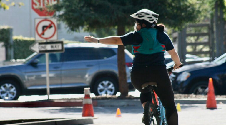 Bike Education Participant signals left while riding their bike in a parking lot.