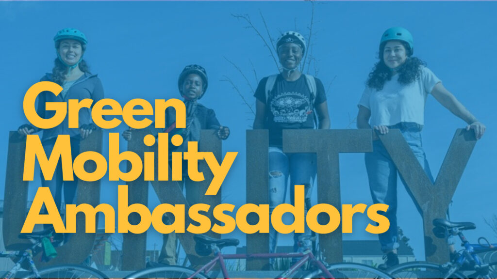"Green Mobility Ambassadors" - Background photo of people wearing bike helmets standing behind a large sign reading "unity"