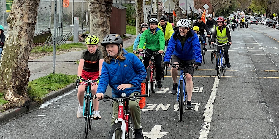 A group of kids with and adults on a group bike ride on the street