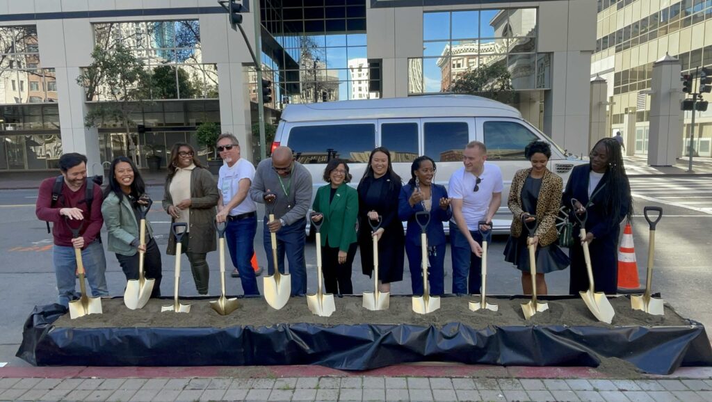 Group of Oakland elected officials and bike advocates standing in a row and digging into the dirt with gold painted shovels