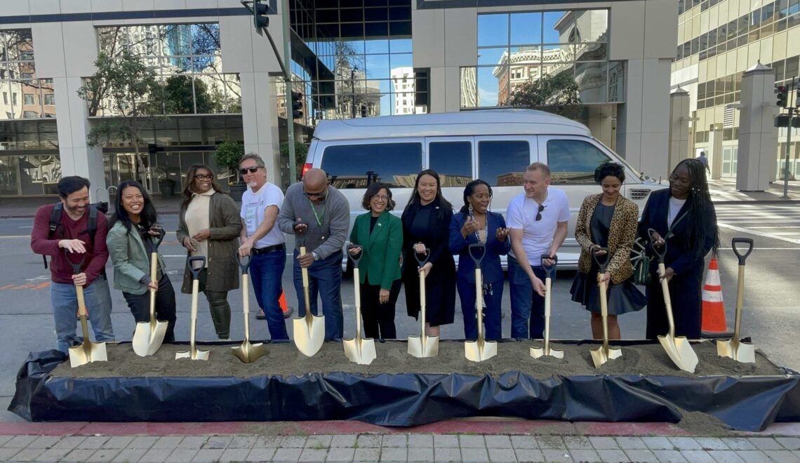 Group of Oakland elected officials and bike advocates standing in a row and digging into the dirt with gold painted shovels