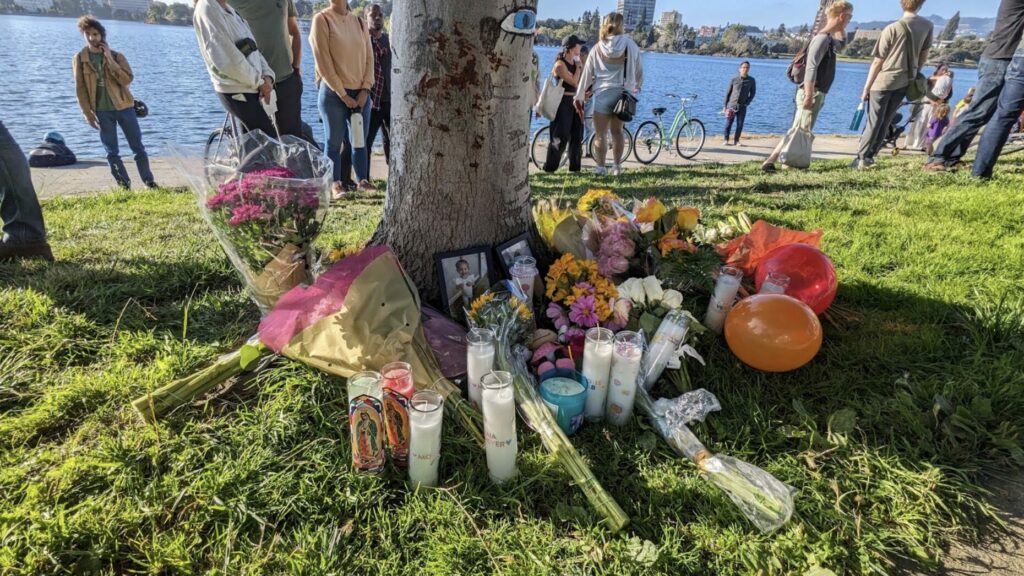 photo of a memorial with flowers photos and candles around a tree at Lake Merritt in Oakland