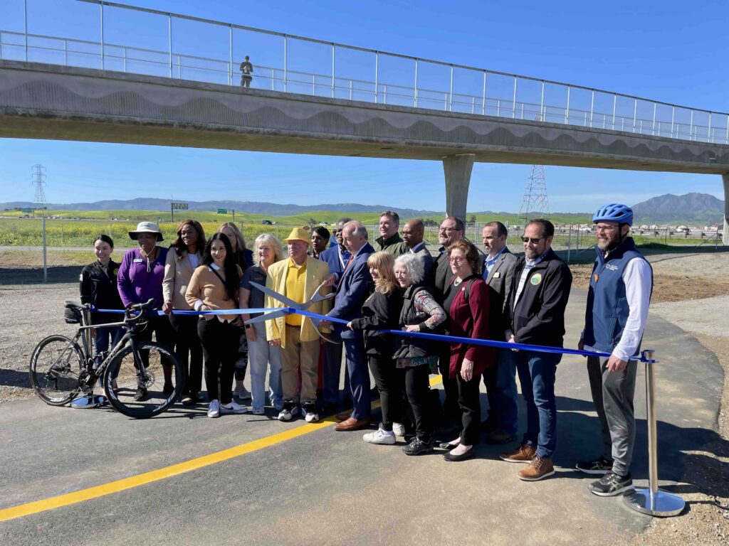 photo of a group of people posing with a ribbon and giant scissors in front of the new Mokelumne Trail Overcrossing