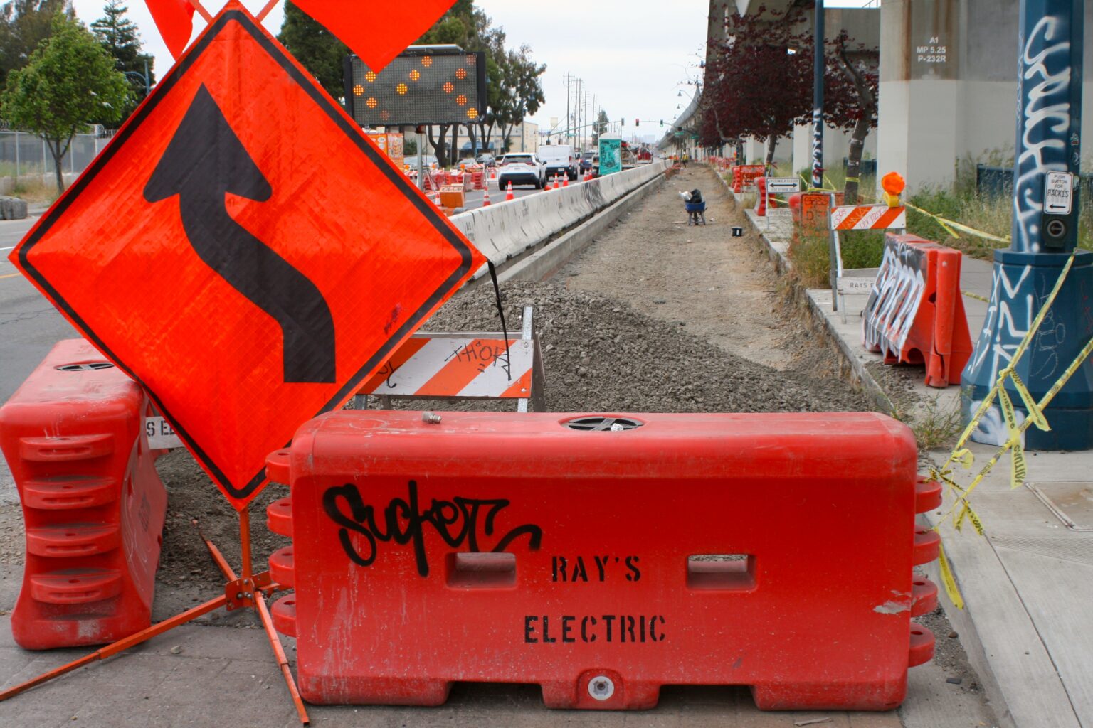 photo of signs and barricades in front of a dug-up construction zone for the East Bay Greenway path on San Leandro St in Oakland