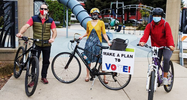 Photo of League of Women Voters bike ride participants posing with their bikes - bike sign reading "make a plan to vote!"