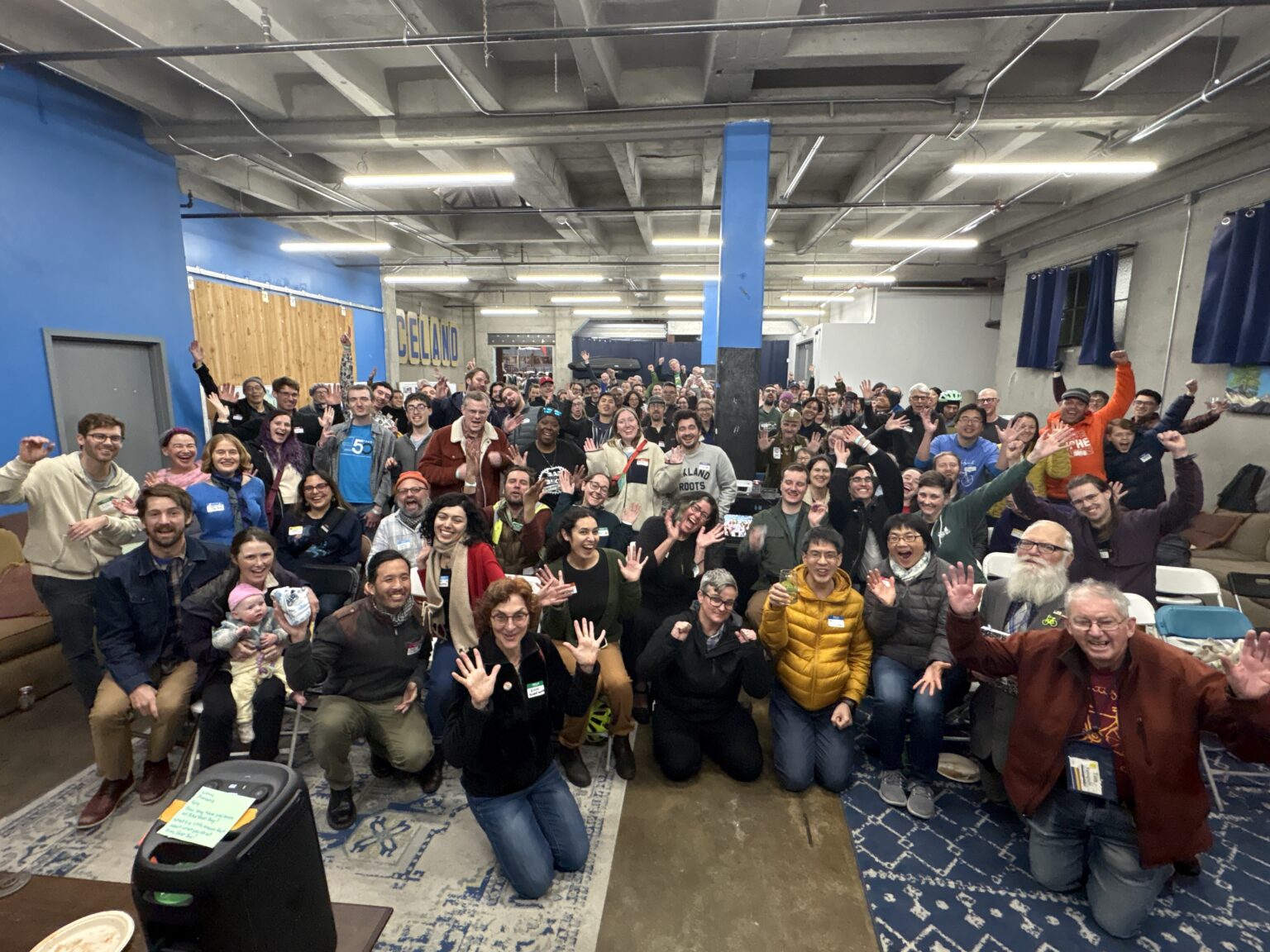 100+ happy people are cheering and posing for a photo at Sports Basement