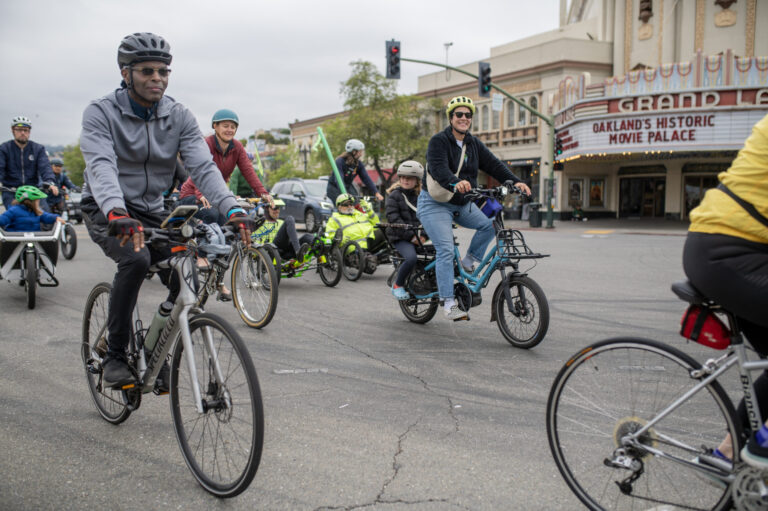 A group of people ride bikes past the historical Grand Lake Theater. BTWD 2024 - Group Ride