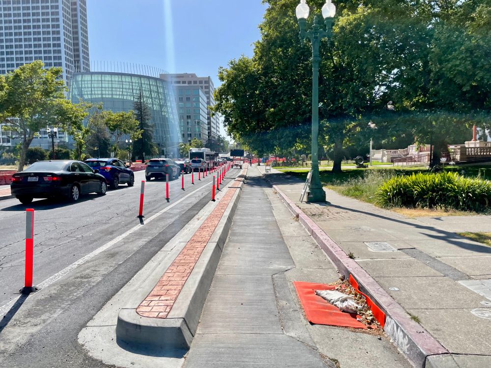 photo of a curbside protected bikeway under construction on Grand Ave approaching Harrison Street in Downtown Oakland