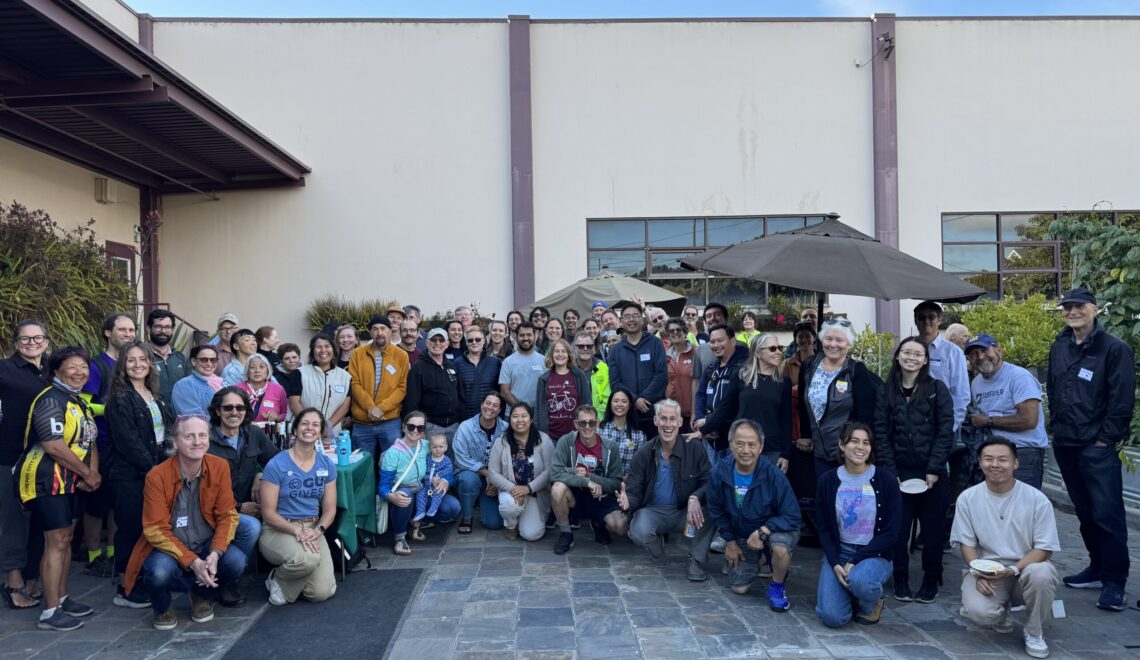 Group photo of about 60 people smiling in the GU Backyard, all dressed in relaxed summer outfits