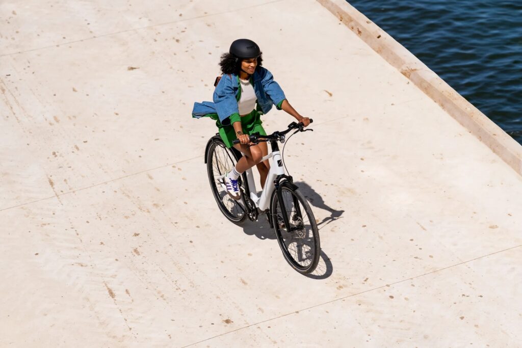 photo from above, looking down at a young person wearing a bike helmet and riding an electric bike on a wide smooth trail along a waterway