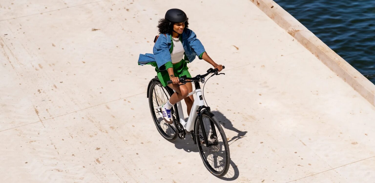 photo from above, looking down at a young person wearing a bike helmet and riding an electric bike on a wide smooth trail along a waterway