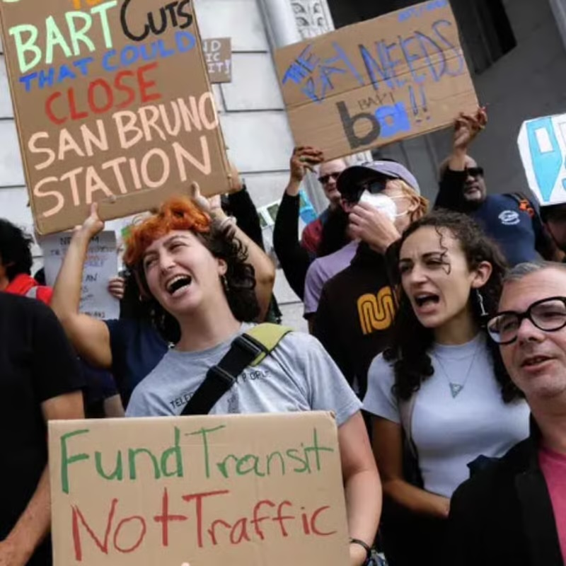 photo of a crowd of protestors shouting and holding signs in support of funding public transit