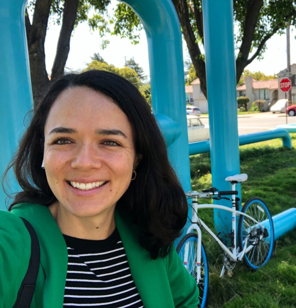Estrella smiles in front of an Albany metal sculpture, with her bike in the background