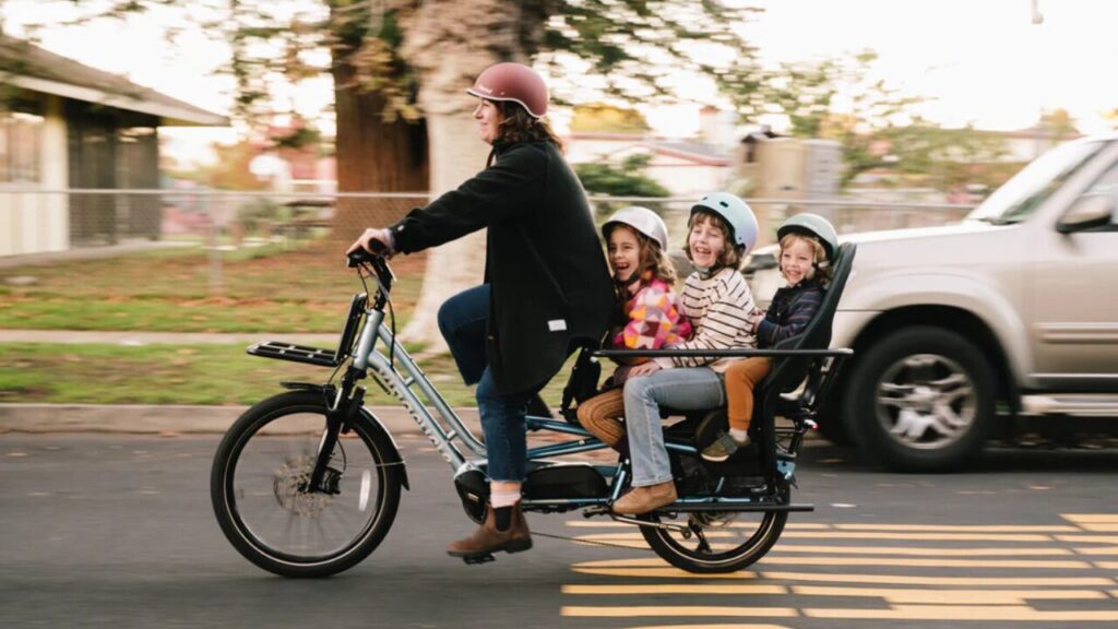A parent transports 3 young kids on the back of her Xtracycle Class 3 Swoop ASM family cargo e-bike.