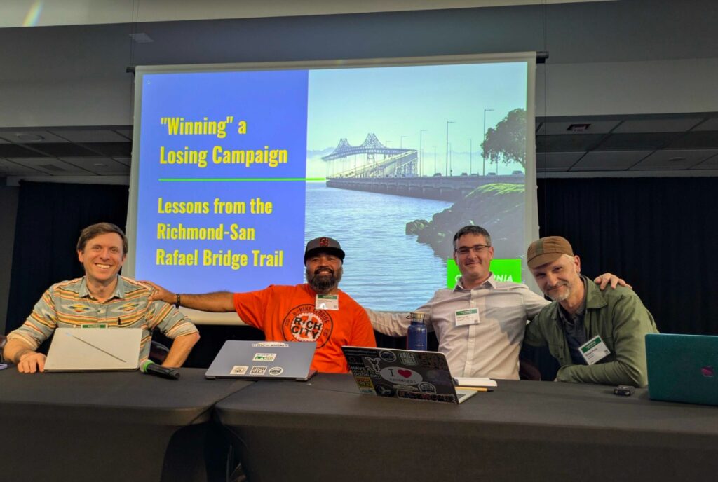 A group of panelists sit in front of a "Winning" a Losing Campaign slide