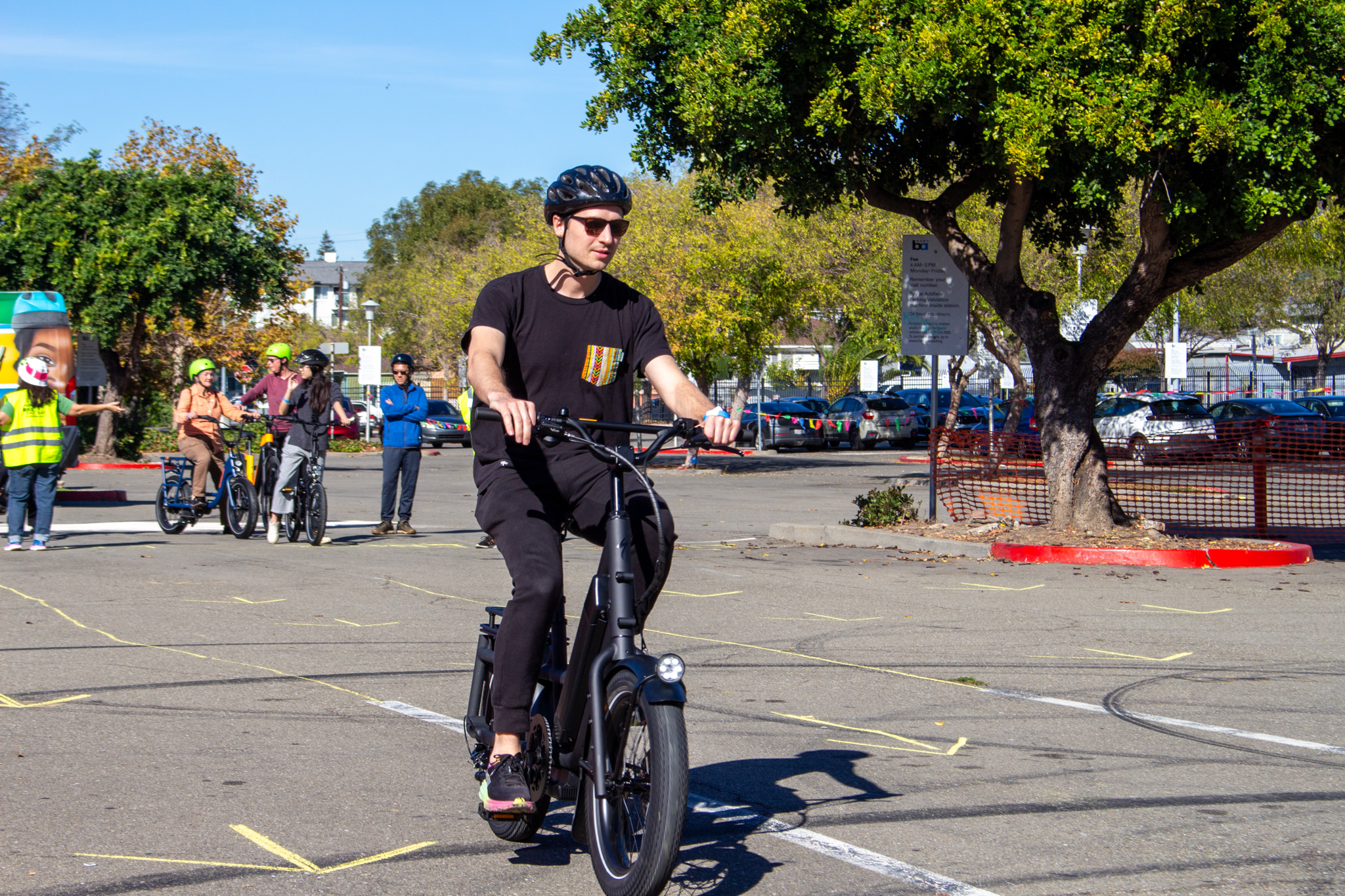 A person dressed in black with a black helmet test rides an e-bike through a parking lot.