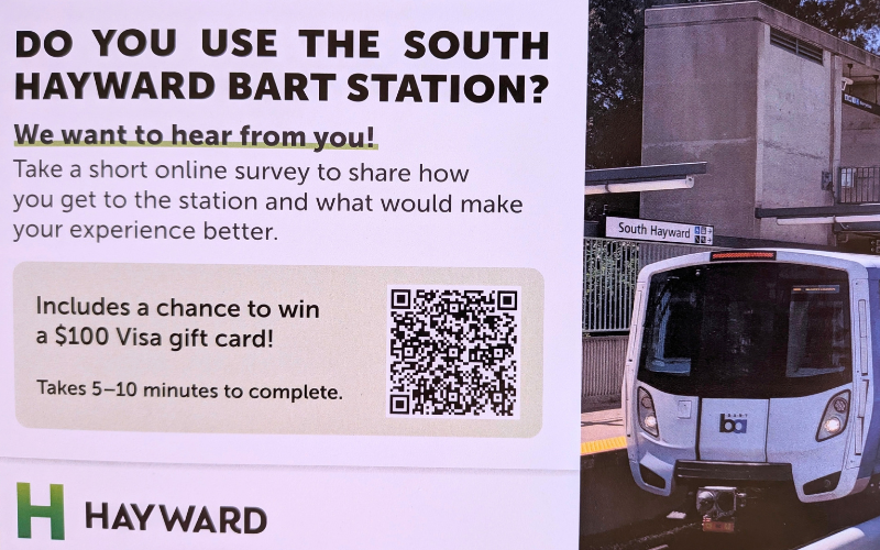 Promotional sign for a City of Hayward survey asking "Do you use the South Hayward BART Station?" next to a photo of a white BART train at the station platform. Link to the survey: https://forms.cloud.microsoft/Pages/ResponsePage.aspx?id=S8p9CMdJxkKnZkmj8p_D9LzVnZ0QNetEhfZfZxFOYO5UNU1UUlhHQU0wUlNFNkVXSkdCRUdOQkFFWS4u&origin=QRCode