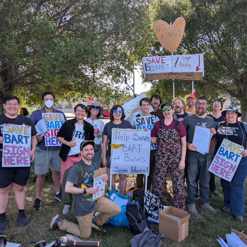 photo of a group of people smiling and posing while holding petition clipboards and signs that read "save BART sign here"