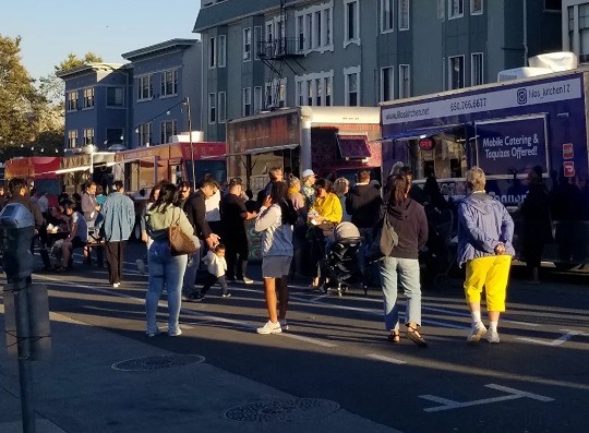 photo of a crowd of people at a block party with food trucks