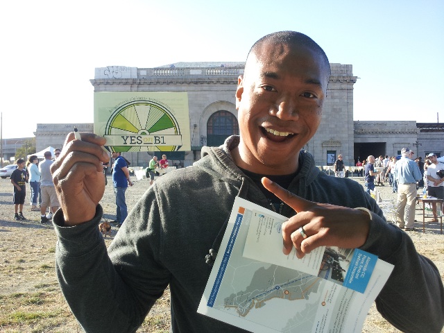 photo of a smiling person holding and pointing to a postcard reading "Yes on B1"